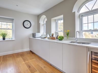 A kitchen with white countertops a sink a microwave toaster bread fruit and flowers on the counter at The Tower 5 Corisande Manor in Newquay