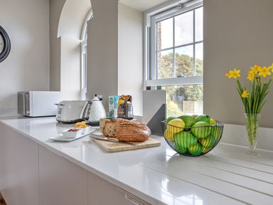 A kitchen counter with bread on a cutting board fruit bowl toaster kettle microwave and flowers at The Tower 5 Corisande Manor in Newquay