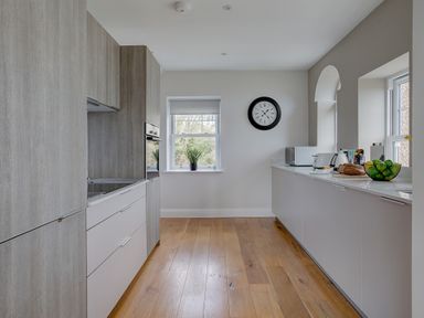 A kitchen with wooden floor cabinets appliances and a clock on the wall at The Tower 5 Corisande Manor in Newquay