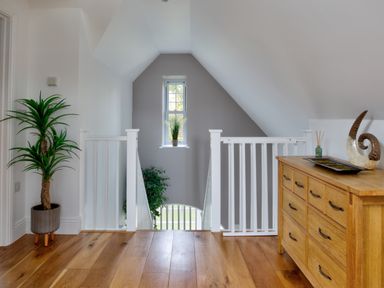 A hallway with wooden flooring a potted plant a wooden dresser and white railings at The Tower 5 Corisande Manor Newquay