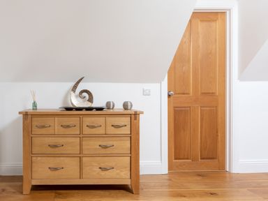 A wooden chest of drawers with decorative items next to a wooden door in a room at The Tower 5 Corisande Manor in Newquay