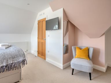 A bedroom with a wooden door a wall-mounted TV a gray chair with a yellow pillow and a bed with folded towels at The Tower 5 Corisande Manor in Newquay