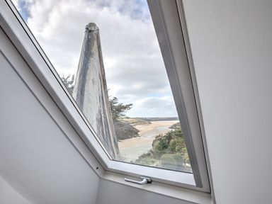 A slanted attic window with a view of a river flowing through a landscape with trees and hills at The Tower 5 Corisande Manor in Newquay