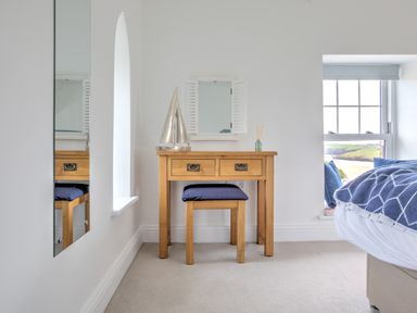 A bedroom with a wooden vanity table and stool beside a window with blue cushions at The Tower 5 Corisande Manor in Newquay
