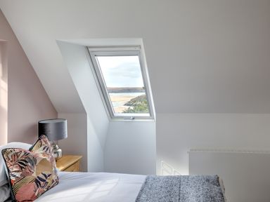 A bedroom with a bed a bedside table a lamp and a window overlooking the coast at The Tower 5 Corisande Manor in Newquay