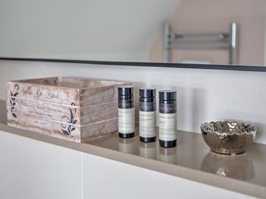 A bathroom shelf with three small toiletry bottles a wooden box and a small metallic bowl at The Tower 5 Corisande Manor in Newquay