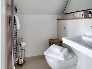 A bathroom with a toilet holding white towels a sink a towel radiator and a wooden box at The Tower 5 Corisande Manor in Newquay