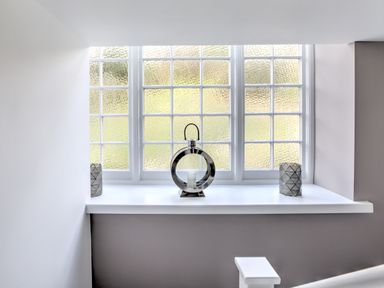 A window with frosted glass panes and three decorative candle holders on the sill at The Tower 5 Corisande Manor in Newquay