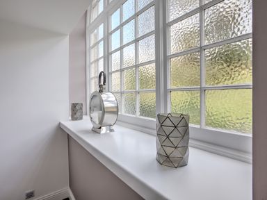 A window with textured glass and a white sill holding two geometric candle holders and a silver lantern at The Tower 5 Corisande Manor in Newquay