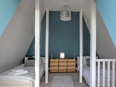 A bedroom with two single beds separated by white beams and a wooden dresser against a blue wall at The Tower 5 Corisande Manor in Newquay