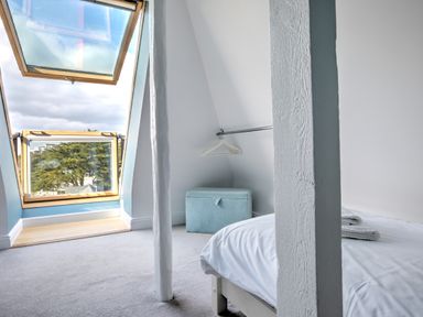 A bedroom with a bed towels a clothing rack with hangers a storage ottoman and a large open skylight window at The Tower 5 Corisande Manor in Newquay