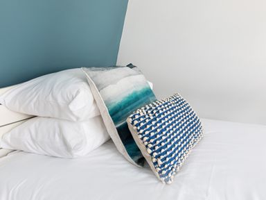 A bed with white pillows and two decorative cushions against a blue and white wall at The Tower 5 Corisande Manor in Newquay