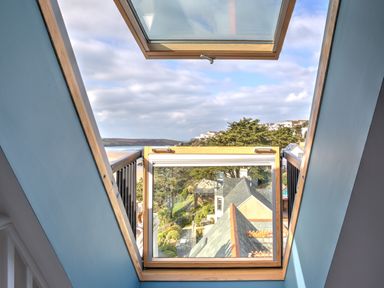 A skylight window with a view of rooftops, trees, and a distant beach at The Tower, 5 Corisande Manor in Newquay