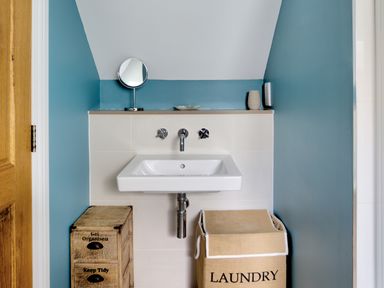 A bathroom sink with faucet and knobs a wooden drawer and a laundry basket under the sink at The Tower 5 Corisande Manor in Newquay
