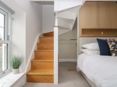Wooden stairs next to a bed with pillows and a built in wooden headboard beside a window with a potted plant at The Tower 5 Corisande Manor in Newquay