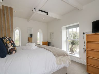A bedroom with a bed with pillows and towels a wooden chest of drawers and windows at The Tower 5 Corisande Manor in Newquay