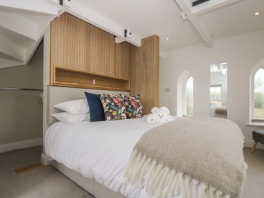 A bedroom with a bed with pillows and folded towels and windows with arched tops at The Tower 5 Corisande Manor in Newquay