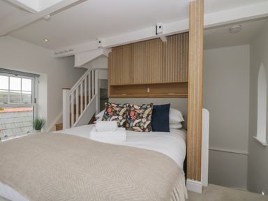 A bedroom with a bed pillows and folded towels near a staircase and window at The Tower 5 Corisande Manor in Newquay