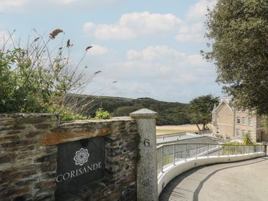 A stone wall with a corisande sign and a driveway leading to a building near the beach at The Tower 5 Corisande Manor in Newquay