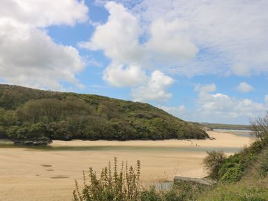 A sandy beach with a small river or creek and green hills under a partly cloudy sky at The Tower 5 Corisande Manor Newquay