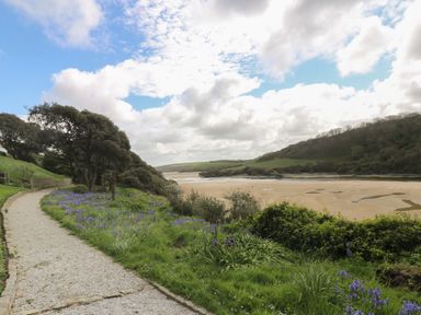 A gravel pathway with trees and purple flowers beside a sandy beach and hills in the background at The Tower 5 Corisande Manor in Newquay