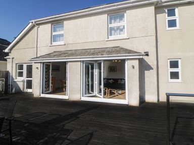 A house exterior with open bi-fold doors leading to a wooden deck at Estuary View in Newton Ferrers