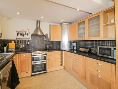 A kitchen with wooden cabinets black tile backsplash and stainless steel appliances at Estuary View in Newton Ferrers