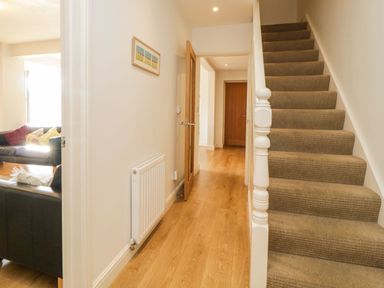 A hallway with wooden floor a staircase on the right and a door to a living room with sofas at Estuary View in Newton Ferrers