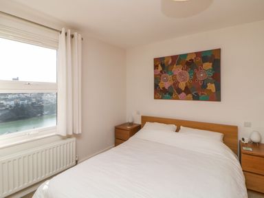 A bedroom with a double bed white bedding wooden headboard two wooden bedside tables with lamps and a colorful framed artwork on the wall at Estuary View in Newton Ferrers