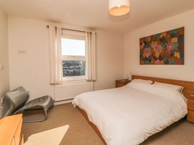 A bedroom with a double bed a chair a window with curtains and a colorful painting on the wall at Estuary View in Newton Ferrers
