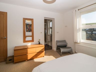 A bedroom with a wooden dresser mirror and gray chair next to a window at Estuary View in Newton Ferrers