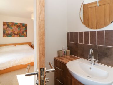 A bedroom with a bed and an abstract painting visible through a partially open door leading to a bathroom with a sink mirror and wooden cabinet at Estuary View in Newton Ferrers