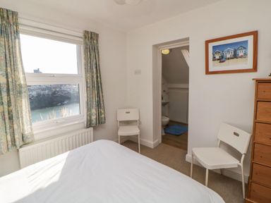 A bedroom with a bed two white chairs a wooden chest of drawers and a window with curtains at Estuary View in Newton Ferrers
