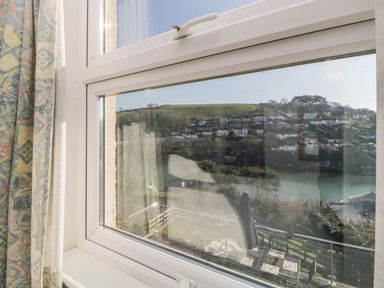 A view through a window showing a hillside with houses and a river at Estuary View in Newton Ferrers