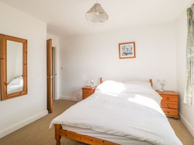A bedroom with a wooden bed and nightstands with lamps a mirror on the wall and a framed picture above the bed at Estuary View in Newton Ferrers