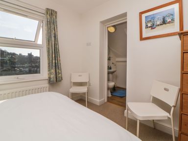 A bedroom with two white chairs a wooden dresser and an open door showing a bathroom at Estuary View in Newton Ferrers