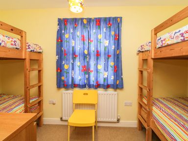 A bedroom with two wooden bunk beds a yellow chair and a window with floral curtains at Estuary View in Newton Ferrers