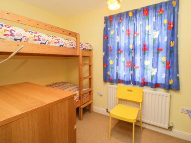 A small bedroom with a wooden bunk bed a yellow chair a wooden chest of drawers and blue floral curtains at Estuary View in Newton Ferrers