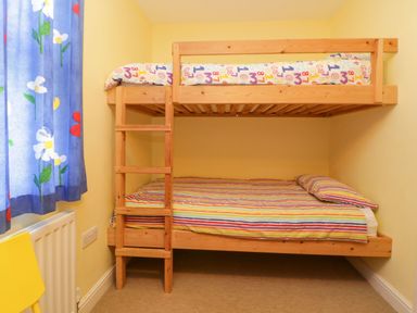 A small bedroom with a wooden bunk bed and colorful bedding near a window with floral curtains