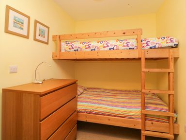 A small bedroom with a wooden bunk bed a wooden chest of drawers and two framed pictures on the wall at Estuary View in Newton Ferrers