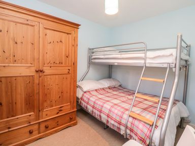 A bedroom with a wooden wardrobe and a metal bunk bed with a plaid blanket at Estuary View in Newton Ferrers