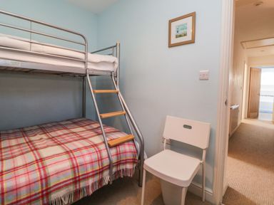 A bedroom with a metal bunk bed with a plaid blanket and a white chair near a hallway at Estuary View in Newton Ferrers
