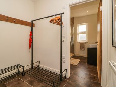 A hallway with a garment rack holding wooden hangers and a red umbrella next to a door leading to a bathroom with a sink and window at Estuary View in Newton Ferrers