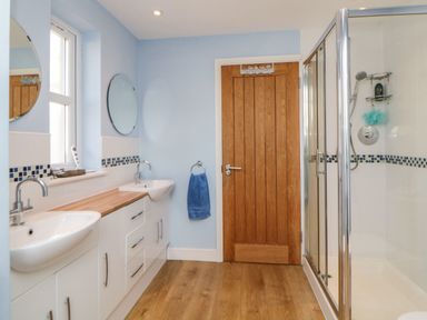 A bathroom with double sinks wooden countertop a wooden door and a glass shower enclosure at Estuary View in Newton Ferrers