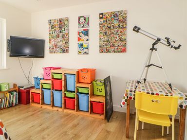 A playroom with colorful storage bins a yellow chair a table with a polka dot tablecloth a telescope and comic book art on the wall at Estuary View in Newton Ferrers