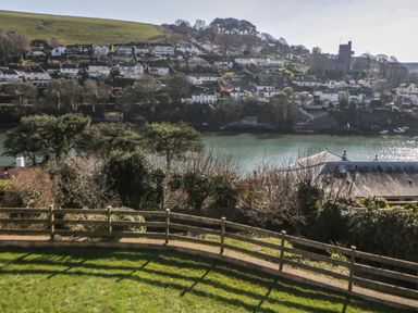 A riverside village with houses on a hillside behind a wooden fence and green lawn at Estuary View in Newton Ferrers