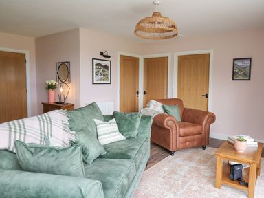 A living room with green and brown sofas wooden doors and a coffee table at Dol Blodau in Newbridge-On-Wye
