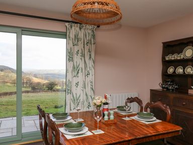 A dining room with a wooden table set for four and a wooden cabinet with plates at Dol Blodau in Newbridge-On-Wye