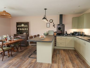 A kitchen and dining area with green cabinets wooden dining table and chairs and an island with bar stools at Dol Blodau in Newbridge-On-Wye