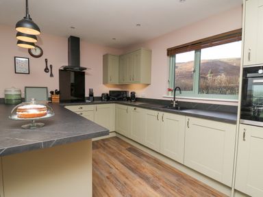 A kitchen with light green cabinets black countertop wooden floor a cake on the counter and a window showing outdoors at Dol Blodau in Newbridge-On-Wye